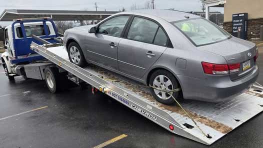 Broken down Hyundai sedan on flatbed tow truck after rod bearing failure.